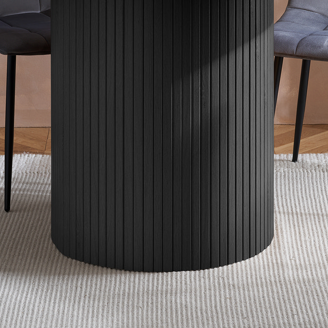 close up image of fluted cylindrical base of black wood effect dining table on soft rug