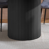 close up image of fluted cylindrical base of black wood effect dining table on soft rug