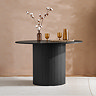 image of round black dining table with fluted cylindrical base, in front of sand coloured wall