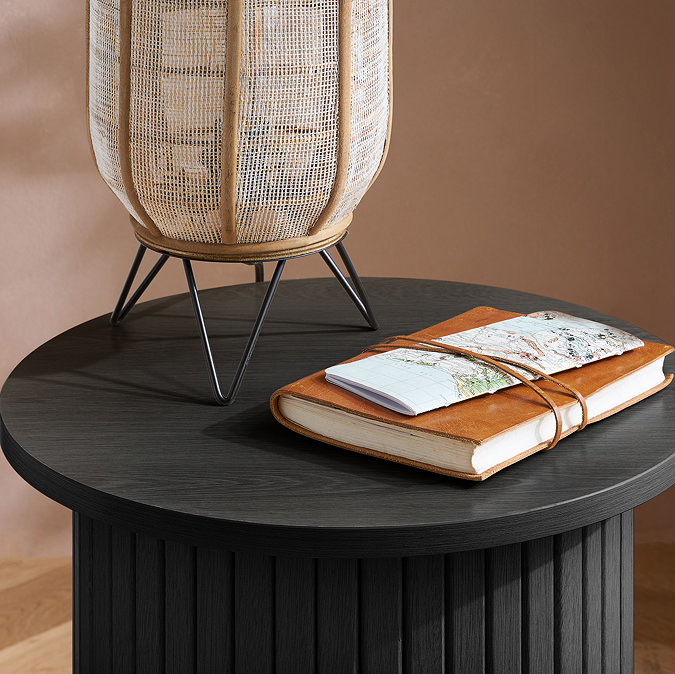 close up image on top of smooth black fluted side table, where a journal and lamp rest on top
