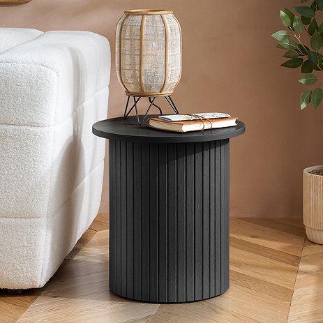image of black fluted wooden side table next to a soft white sofa, with boho lamp on top