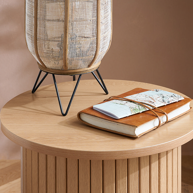 close up image of oak effect round side table with boho lamp and leather journal resting on top
