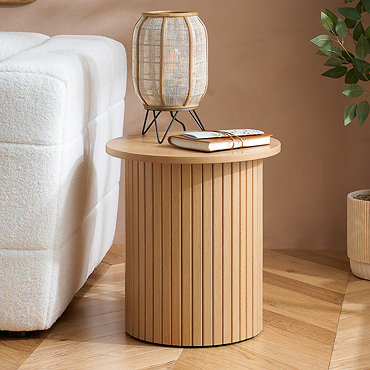 close up image of oak effect round side table with boho lamp and leather journal resting on top