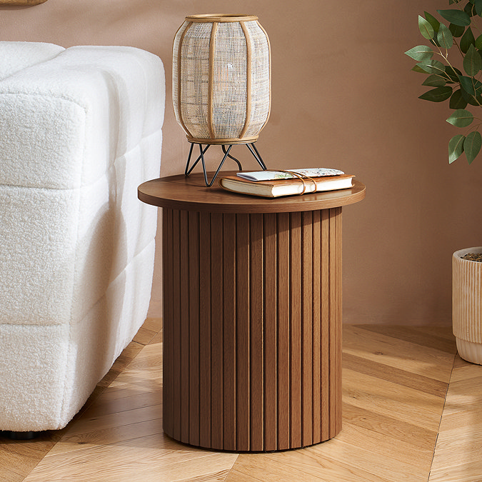 image of walnut coloured side table with fluted detailing on the stand, next to a cream sofa with a rattan lamp on it.