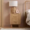 oak fluted bedside table with two drawers, topped with lamp