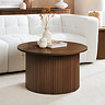 image of round walnut coloured coffee table with slats, in front of a cream sofa on a cream carpet, topped with modern vase and coffee table books.