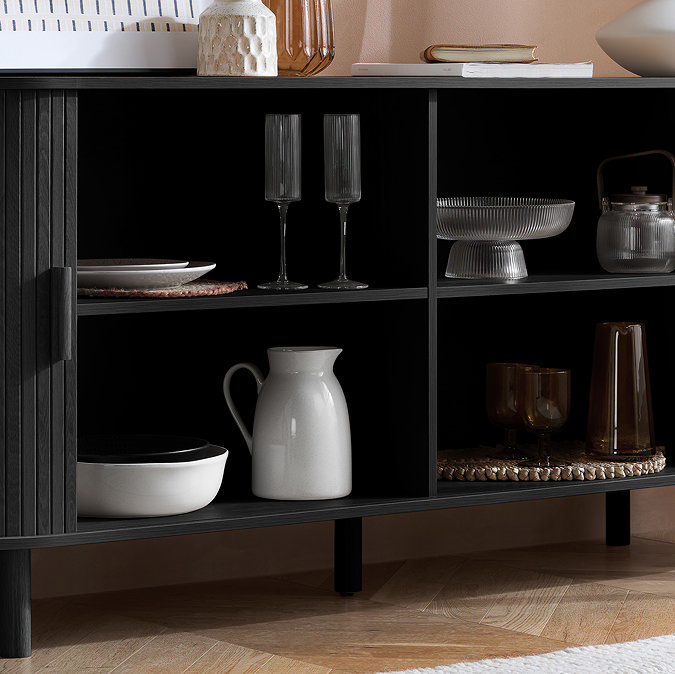 close up image of black wooden sideboard with doors open, showing crockery and dishware on shelved within