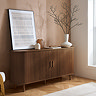 walnut brown sideboard with fluted detailing. two handles on closed doors, with painting and plant on top.