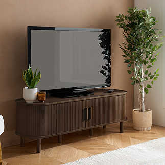 image of walnut wood effect fluted tv stand with tv on top, next to potted plant, with doors shut