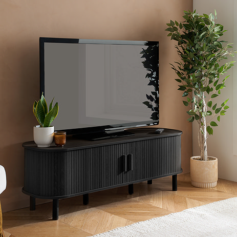 image of black tv stand with tv on top, next to potted plant, with fluted doors closed