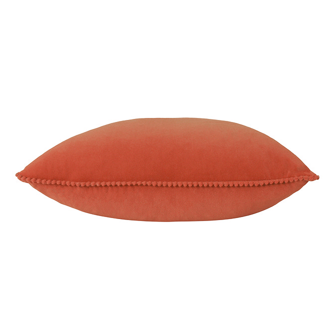 image cut out on white background of brick orange cushion with tiny pom-pom edging, on its side to show its plumpness
