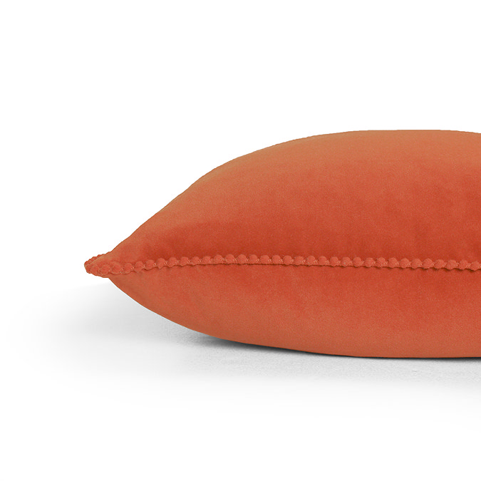 close up image cut out on white background of brick orange cushion with pom pom edges