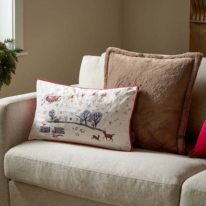 wide shot of rectangular christmas cushion on cream sofa in front of fluffy brown cushion