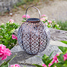 image of round bronze lantern with floral design on stone garden patio