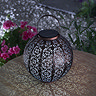 image of round bronze lantern with floral design causing light to spill out in patterns on a table at dusk