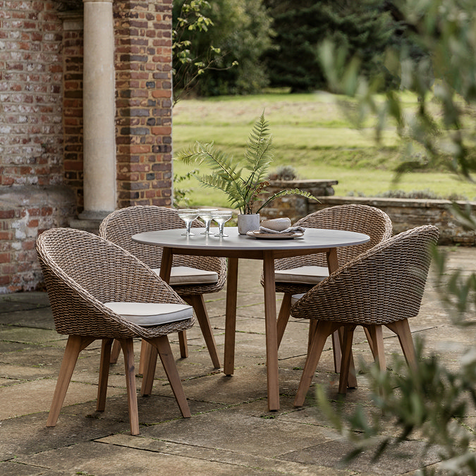 image of four chic wicker seats with cream cushions, tucked into a round table in a garden