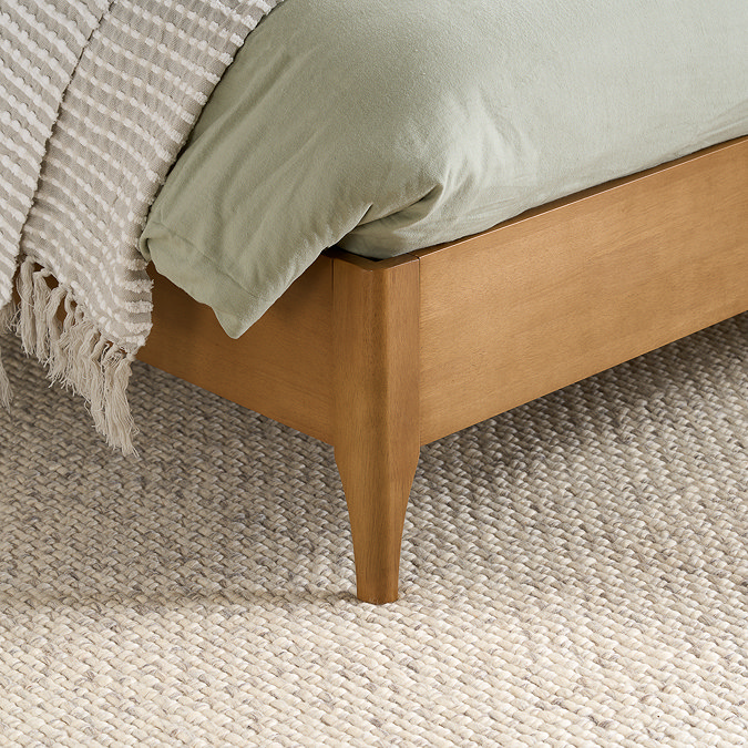 close up image of footboard and thin feet of double bed, natural wood effect, on rug