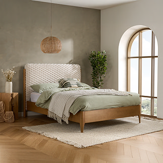 image of natural wood slatted bed with a faux fur bubble headboard, against a grey-green wall of bedroom
