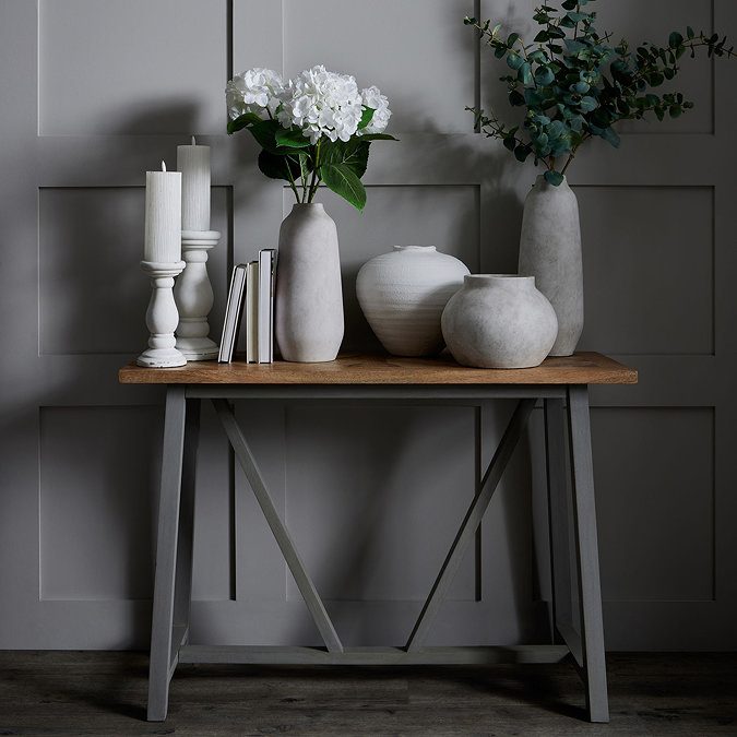 image of grey planter and matching tall vase on a side table in front of a dark grey panelled wall