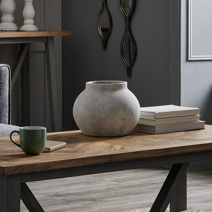 image of large stone planter on a wooden coffee table next to a pile of coffee table books and a forest green mug
