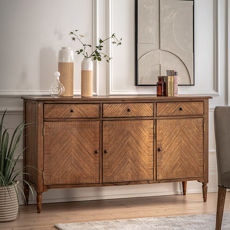 image of mindi wood sideboard with 3 doors and 3 drawers, up against a cream wall in a dining room, topped with decorative acessories