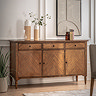 image of mindi wood sideboard with 3 doors and 3 drawers, up against a cream wall in a dining room, topped with decorative acessories