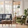 wide image of round natural wooden coffee table in living room, in front of velvet sofa and green armchair