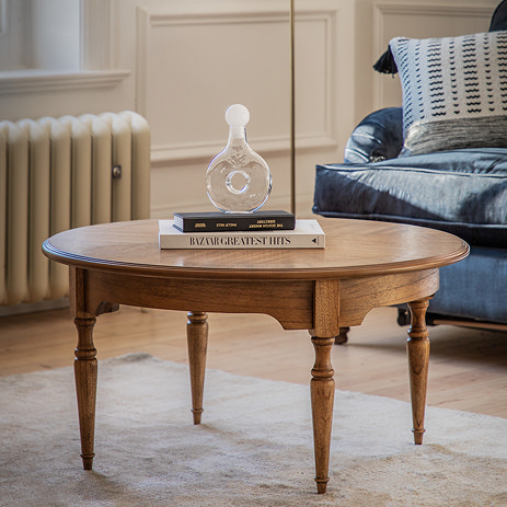 image of natural wood round coffee table with thin legs on neutral rug in a living room