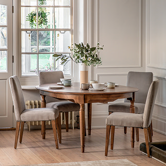 image of round mindi wood dining table with upholstered grey velvet dining chairs around it, on wood flooring of dinign room