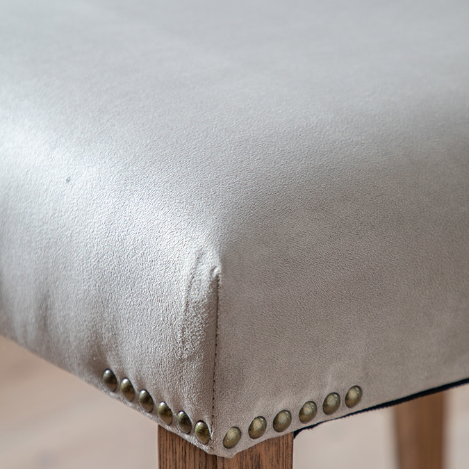 close up image of grey velvet material of dining chair, with subtle brass studs at the point where the material meets the mindi wood legs