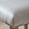 close up image of grey velvet material of dining chair, with subtle brass studs at the point where the material meets the mindi wood legs