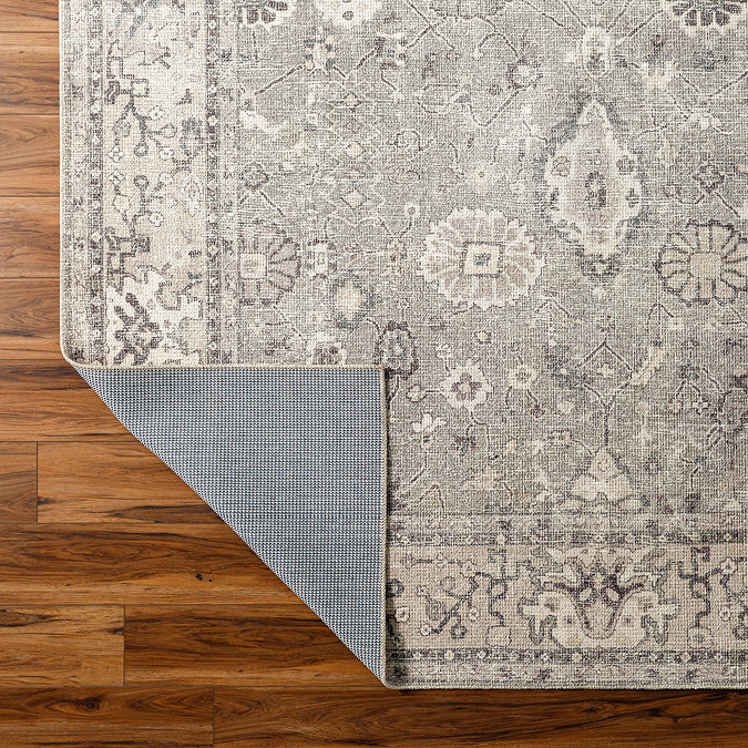 close up image of grey floral rug with corner folded over slightly to reveal material underneath