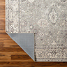 close up image of grey floral rug with corner folded over slightly to reveal material underneath