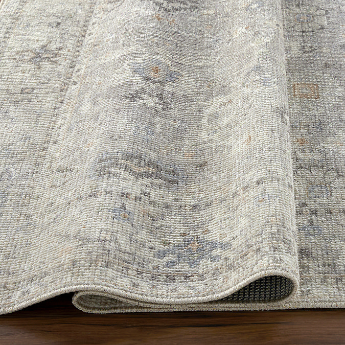 close up image of grey floral vintage rug folded up to suggest its thinness