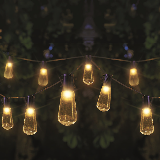 image of decorative warm white bulbs hanging between trees at night, emitting light