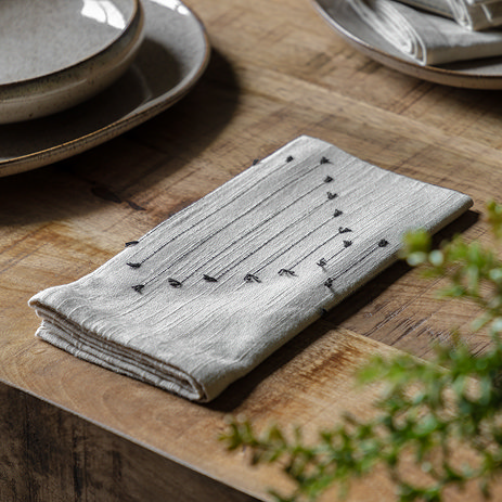 image of folded linen napkin with embroidered abstract pattern, on wooden dining table next to ceramic plate