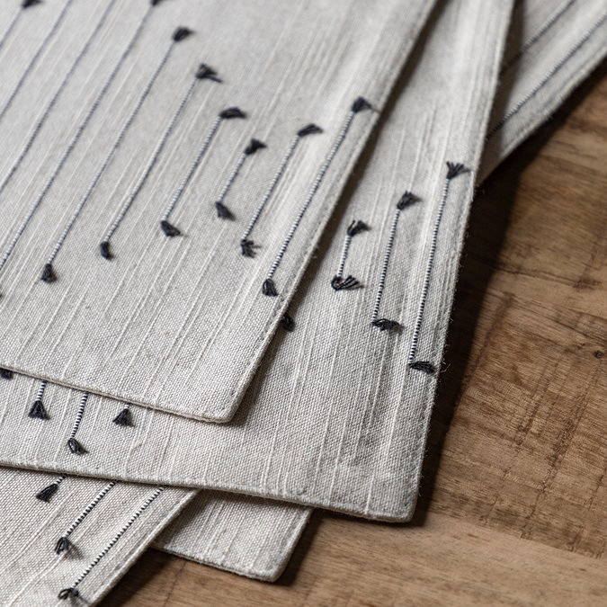 close up image of linen placemats with black diamond pattern weave, pack piled up on top of each other on dark oak table
