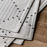 close up image of linen placemats with black diamond pattern weave, pack piled up on top of each other on dark oak table