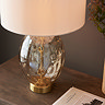 close up image on dimpled champagne gold body of table lamp, warmly lit by bulb inside, on a warm wooden side table