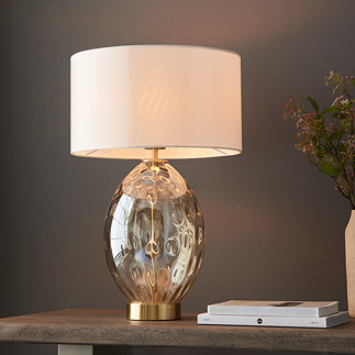 image of table lamp with champagne gold dimpled body and linen shade, bulb inside turned on to emit warm glow