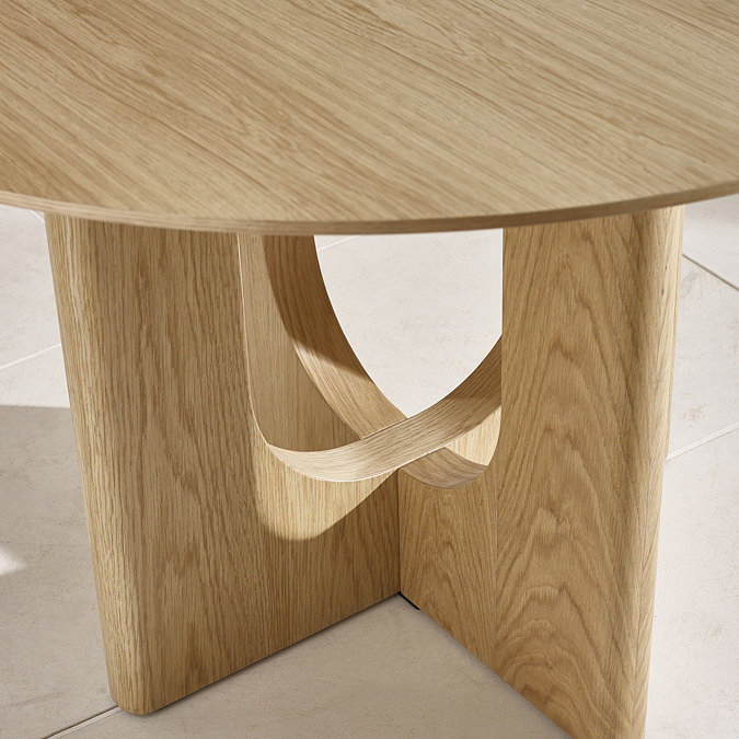 close up image of round oak dining table with cross legs, highlighting form and texture