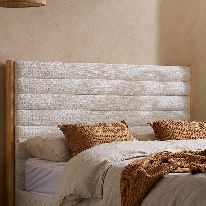 close up image of plush light grey fabric headboard of light wood bed