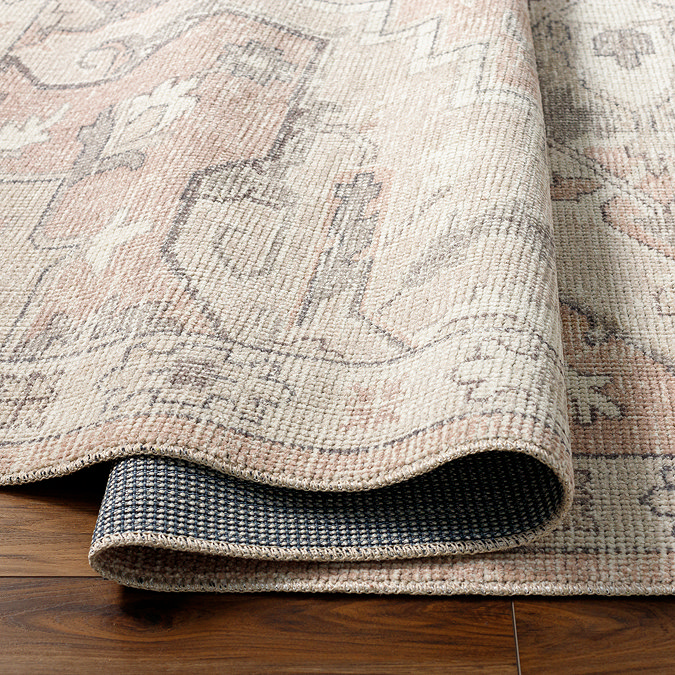 close up image of tan coloured rug with vintage patterns, ruched up slightly to show its thinness