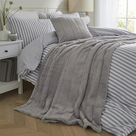 grey faux fur throw draped over light blue striped bedding