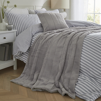 grey faux fur throw draped over light blue striped bedding