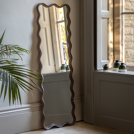 image of dark wood wiggle leaner mirror against a light grey wall next to potted plant