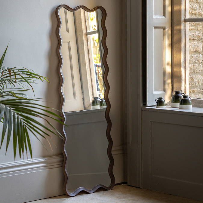 image of dark wood wiggle leaner mirror against a light grey wall next to potted plant