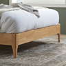 close up on wooden feet of a double bedframe, light oak colour, resting on a patterned rug in a bedroom