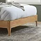 close up on wooden feet of a double bedframe, light oak colour, resting on a patterned rug in a bedroom
