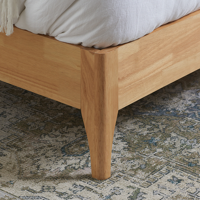 close up on slim feet of light oak bed resting on patterned rug